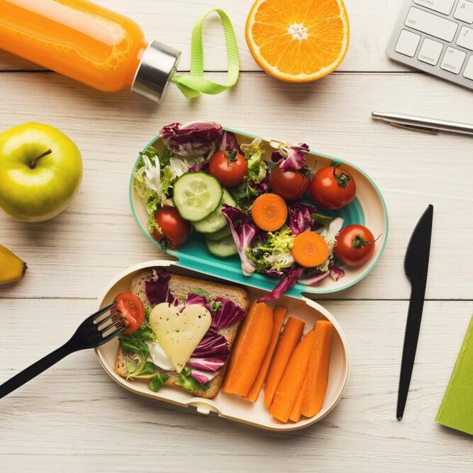Healthy work lunch Healthy packed lunch with salad, vegetables and fruit next to a laptop