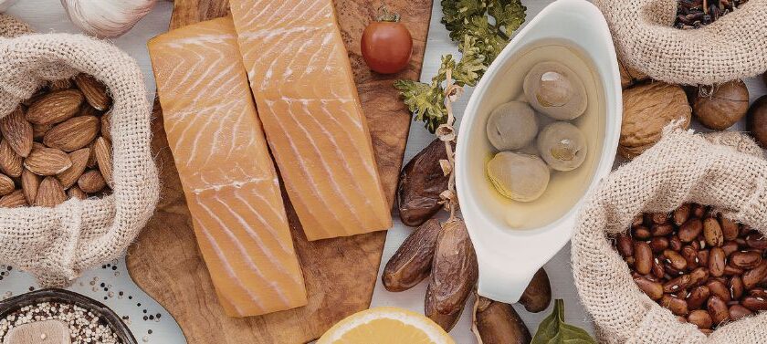 Mediterranean diet foods for perimenopause including salmon, nuts, eggs, legumes, olive oil and lemon on wooden board