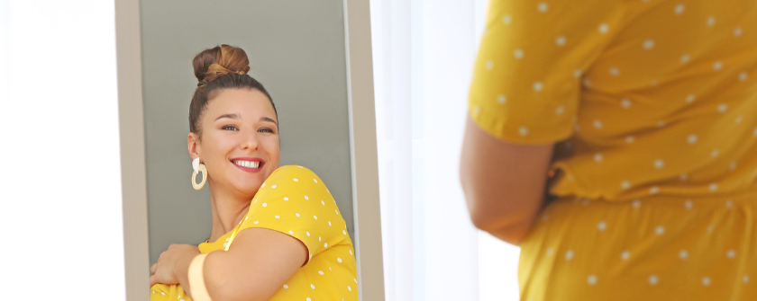 Smiley woman in yellow dress looking into mirror